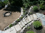 Stone steps descending through retaining wall to a rock ring firepit