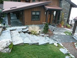 Lawn slope leading up to stone steps leading down to gravel and paver pathway