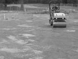 Using a roller to smooth and compact a surface prior to hardscape installation